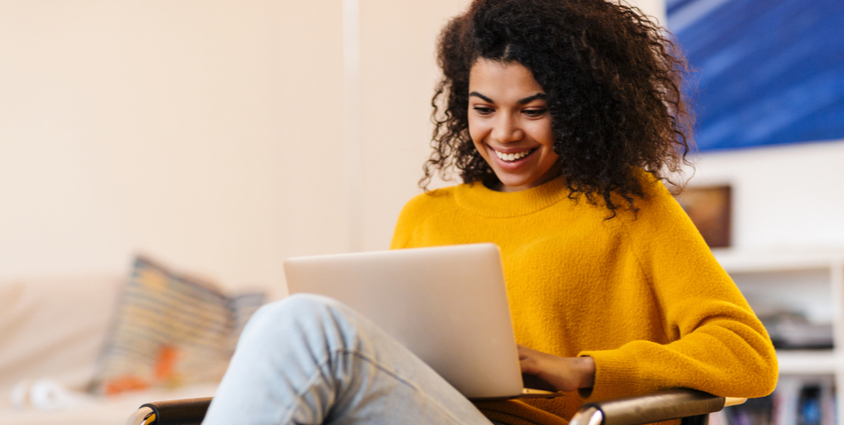 Cheerful woman using laptop while sitting on chair in living room