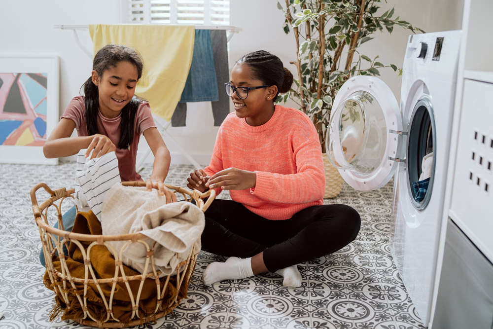 Girls folding clothes in basket next to dryer