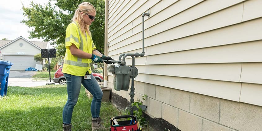 Female employee working at a gas meter on the side of a house that has beige siding