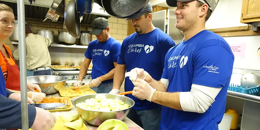 3 male employees with blue Columbia Cares volunteer shirt volunteering at soup kitchen