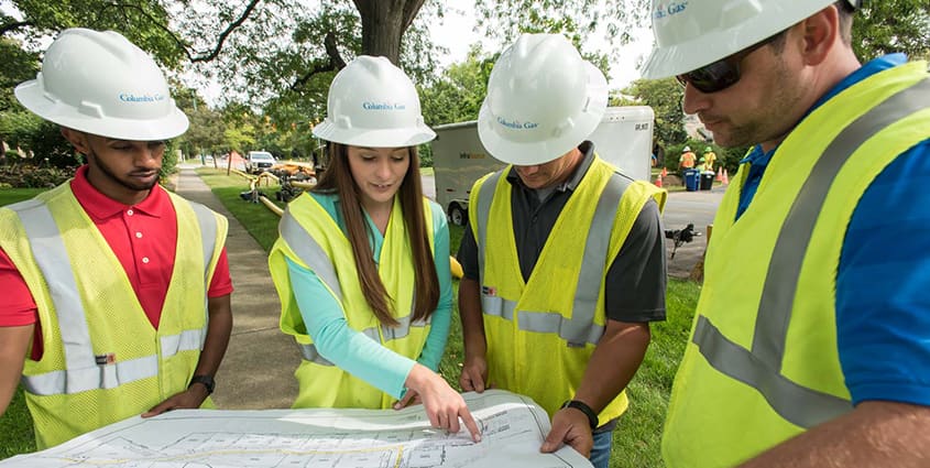 4 Employees with hard hats  working in the field together looking at a map