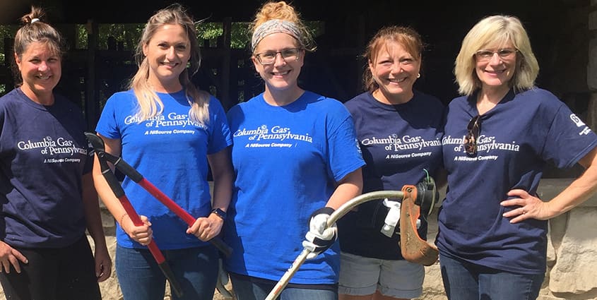 Pennsylvania employees wearing Columbia Gas volunteer shirts and holding up garden tools